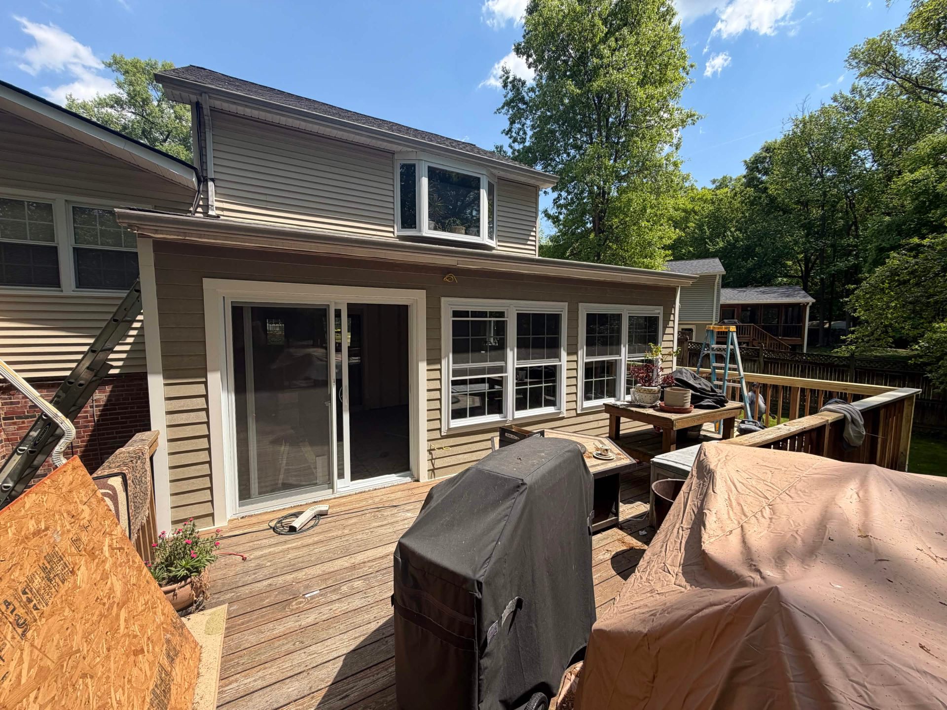 After photo of the same home with a finished one-story addition built where the covered deck used to be — new tan siding and white trim, a four-window bank, a sliding patio door, and a tied-in shingle roofline matching the existing house.