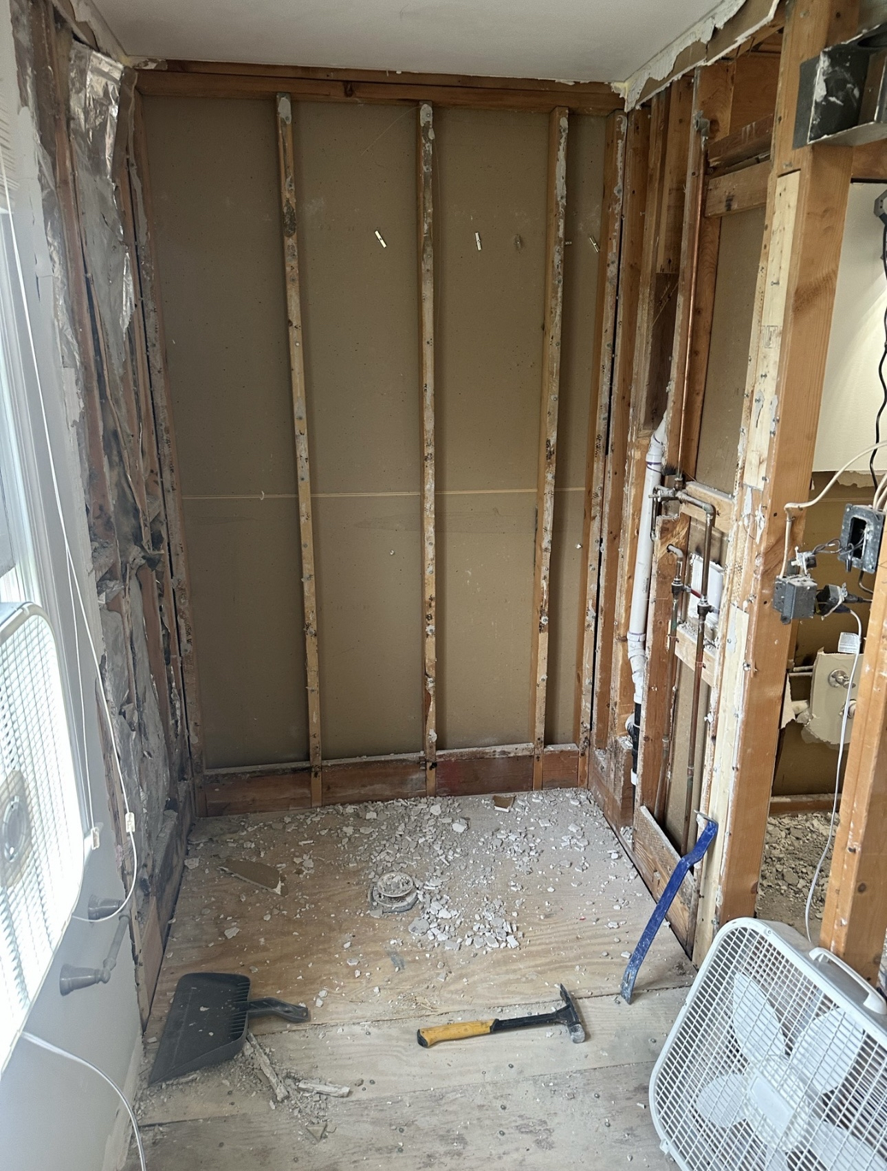 In-progress demo of a bathroom taken down to the studs, with exposed framing, new plumbing rough-in for a walk-in shower, and visible electrical boxes.