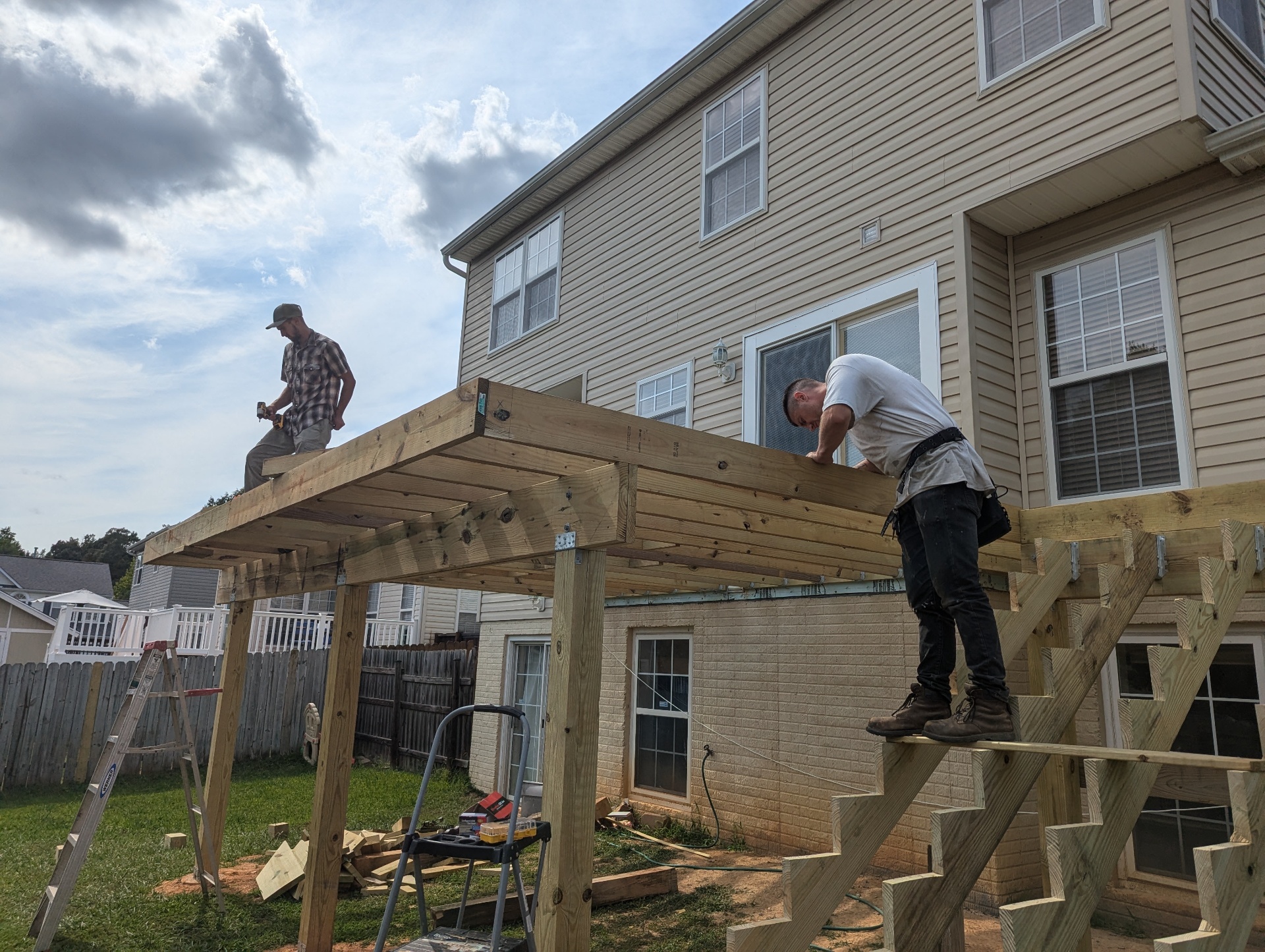 Two carpenters from the Perpetual Improvements crew installing pressure-treated floor joists on a custom elevated deck frame at the back of a residential home.