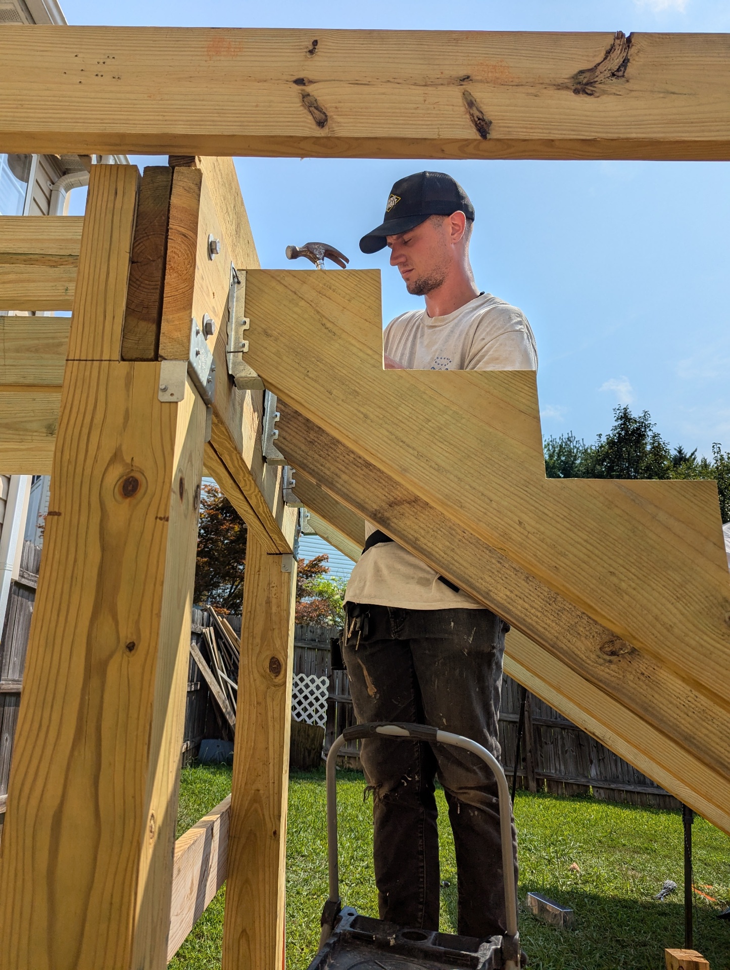 Carpenter framing custom-cut pressure-treated stair stringers on-site during construction of an elevated backyard deck.