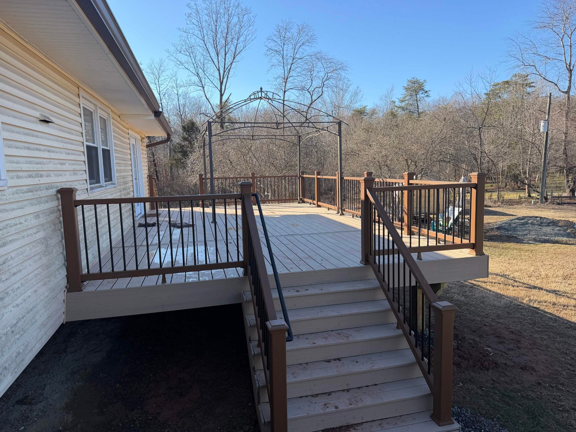 Rebuilt back deck with two-tone composite decking, brown composite top rail, and a wide staircase descending to the backyard of a single-story home.