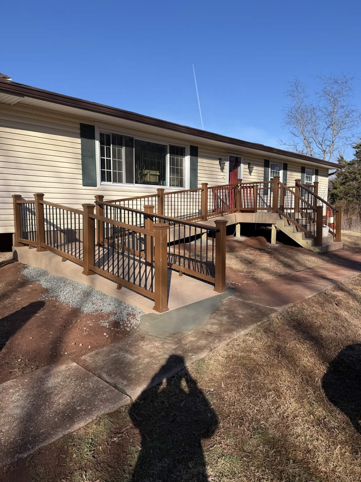 Newly rebuilt front entry deck on a single-story ranch home with two-tone tan composite decking, brown composite railing, and black aluminum balusters wrapping around to a side staircase.