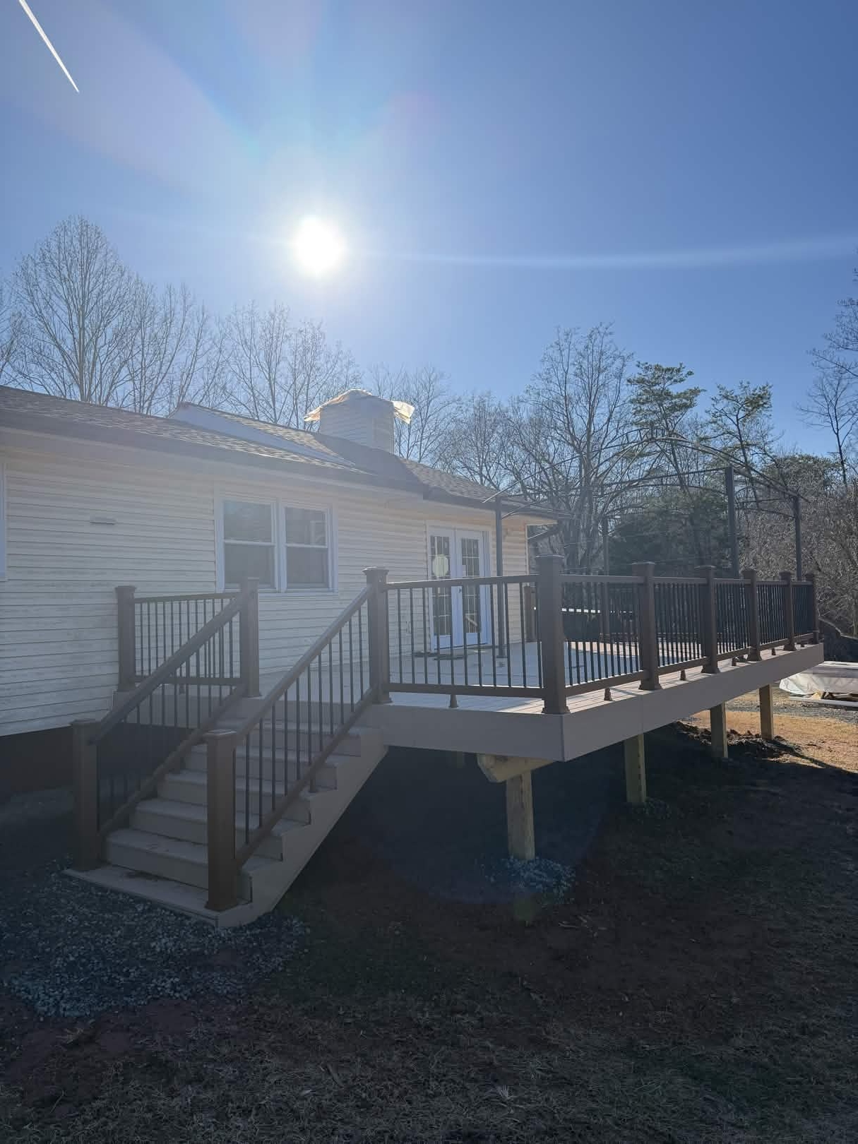 Side angle of a rebuilt back deck on a single-story home, showing the elevated composite platform, brown railing system, and side staircase descending to the yard.